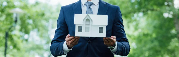 Panoramic shot of young businessman holding house layout while standing in park — Stock Photo