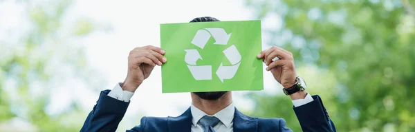 Panoramaaufnahme eines Geschäftsmannes, der im Park eine Karte mit Recyclingschild hält — Stockfoto