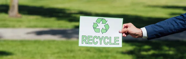 Panoramaaufnahme eines Mannes, der im Park eine Karte mit Recyclingschild hält — Stockfoto