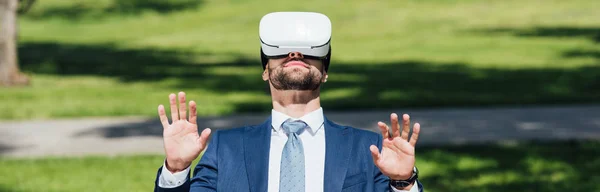 Panoramic shot of businessman gesturing in park witn VR headset — Stock Photo