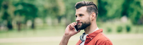 Panoramic shot of man talking on smartphone while standing in park — Stock Photo