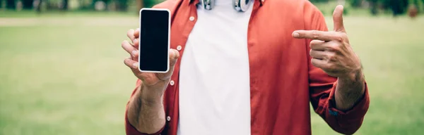 Panoramaaufnahme eines Mannes, der mit dem Finger auf ein Smartphone mit leerem Bildschirm zeigt — Stockfoto