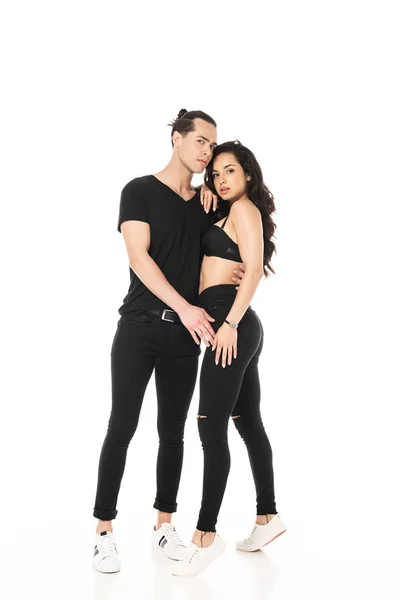 Visão de comprimento total do casal em roupas pretas abraçando e olhando para a câmera isolada no branco — Fotografia de Stock