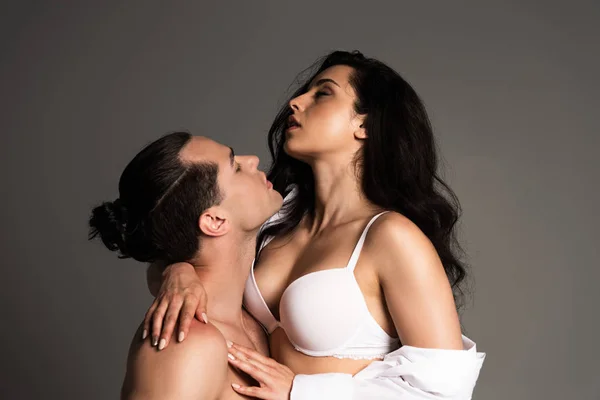 Сексуальна без сорочки брюнетка чоловік обіймається з привабливою подругою ізольовано на сірому — стокове фото