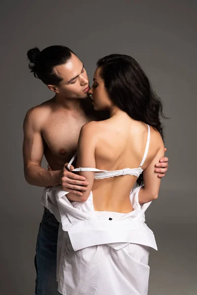 Без сорочки молодий чоловік обіймається з сексуальною дівчиною ізольовано на сірому — стокове фото
