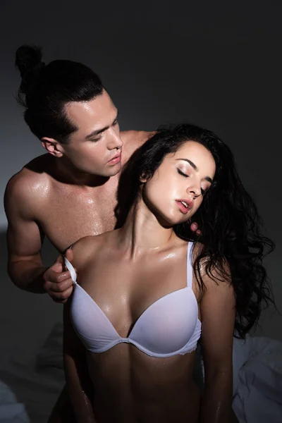 Camicetta uomo spogliarsi fidanzata sexy mentre seduto sul letto in camera da letto scuro — Foto stock