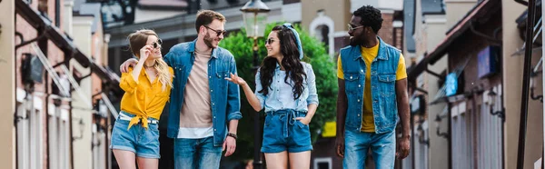 Panoramic shot of cheerful woman with hand in pocket gesturing near multicultural friends — Stock Photo
