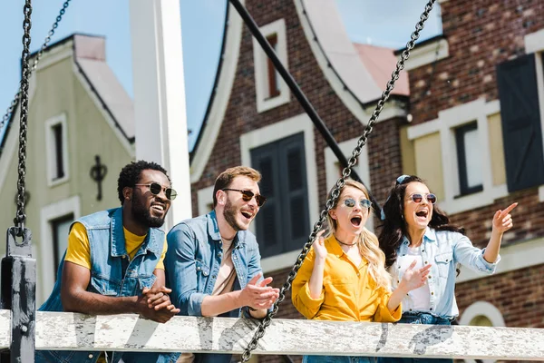 Cheerful woman pointing with finger near surprised girl and multicultural friends — Stock Photo
