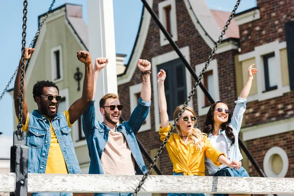 Alegre grupo de amigos multiculturales en gafas de sol celebrando el triunfo - foto de stock