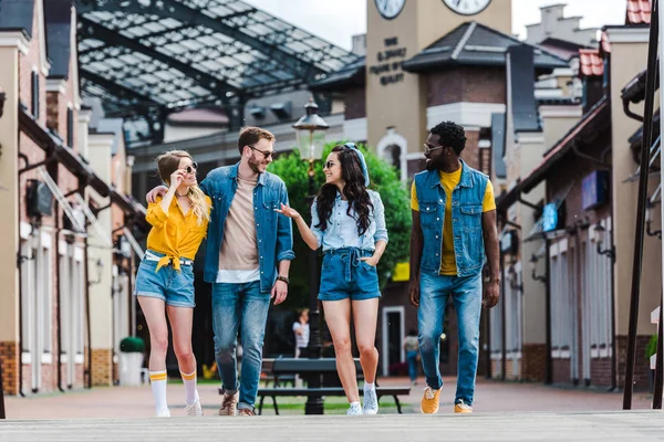 Cheerful woman with hand in pocket gesturing while walking near multicultural friends — Stock Photo