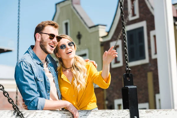 Mujer alegre en gafas de sol señalando con el dedo cerca de hombre guapo - foto de stock