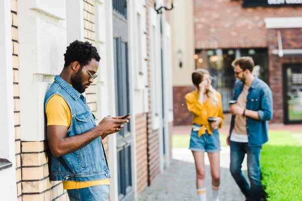 Messa a fuoco selettiva di bello afro-americano uomo in occhiali da sole utilizzando smartphone al di fuori — Foto stock