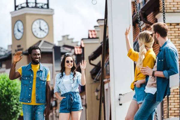 Foco seletivo de amigos multiculturais felizes acenando as mãos e sorrindo fora — Fotografia de Stock