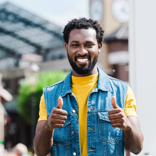 Feliz afroamericano hombre mostrando los pulgares hacia arriba mientras mira la cámara - foto de stock