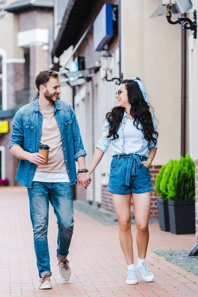 Mujer feliz con la mano en el bolsillo caminando y tomados de la mano con el hombre - foto de stock