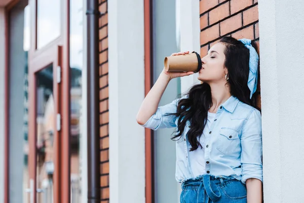 Attraktive junge Frau trinkt Kaffee to go, während sie draußen steht — Stockfoto