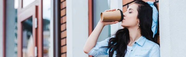Plan panoramique de jeune femme attrayante buvant du café pour aller tout en se tenant dehors — Photo de stock