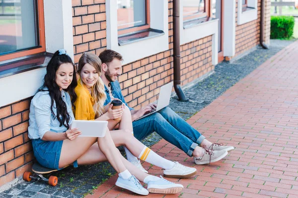 Happy women using digital tablet while sitting on penny board near man with laptop — Stock Photo