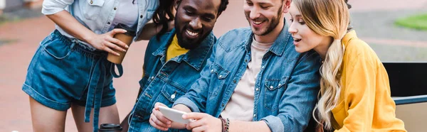 Plano panorámico de amigos multiculturales felices mirando el teléfono inteligente - foto de stock