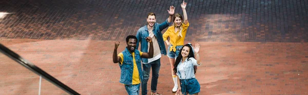 Plano panorámico de amigos multiculturales felices haciendo gestos mientras están de pie juntos — Stock Photo