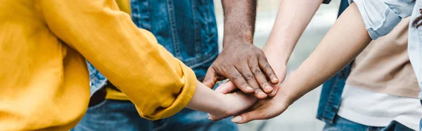 Panoramic shot of multicultural friends putting hands together — Stock Photo