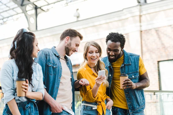 Fröhliche multikulturelle Freunde, die beim Zusammenstehen aufs Smartphone schauen — Stockfoto