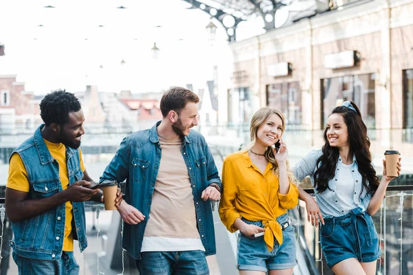 Mujer alegre hablando en el teléfono inteligente cerca de amigos multiculturales - foto de stock