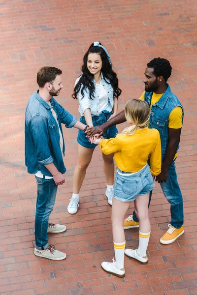 Overhead view of cheerful multicultural friends putting hands together — Stock Photo