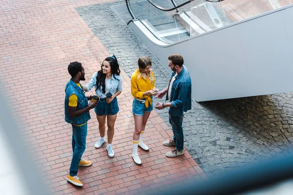 Blick von oben auf fröhliche multikulturelle Freunde, die im Stehen mit Einwegbechern reden — Stockfoto