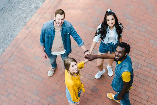 Overhead view of happy multicultural friends putting hands together and looking at camera — Stock Photo