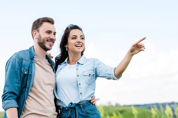 Cheerful and attractive girl smiling while pointing with finger near handsome man — Stock Photo