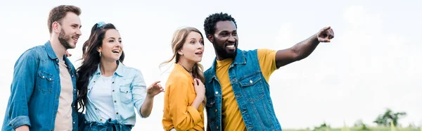 Panoramic shot of happy african american man pointing with finger while standing with friends — Stock Photo