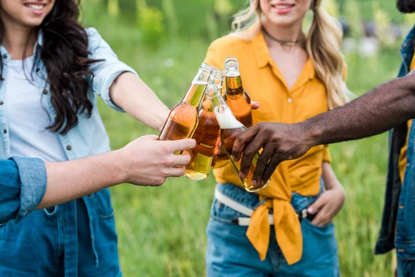 Vista ritagliata di allegri uomini e donne multiculturali clinking bottiglie con birra — Foto stock