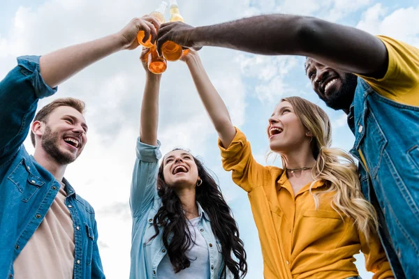 Bottom view of cheerful multicultural women and men clinking bottles with beer — Stock Photo