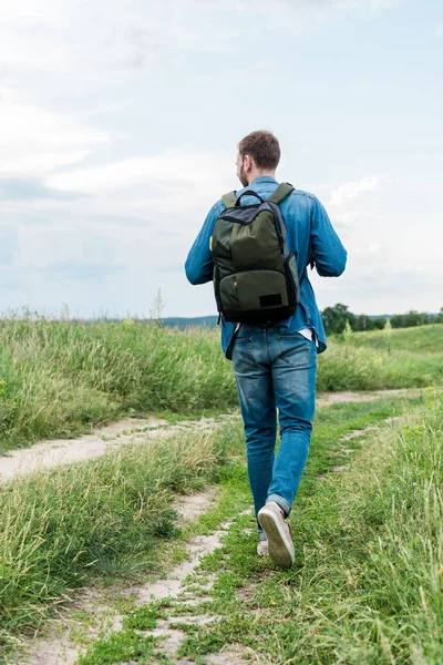 Visão traseira do jovem caminhando com mochila na grama verde — Fotografia de Stock