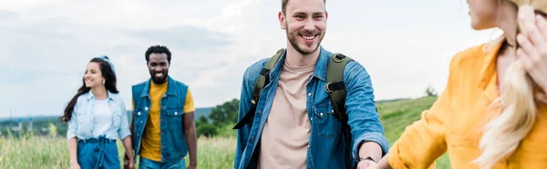 Plano panorámico de la mujer cogida de la mano con el hombre cerca de amigos multiculturales - foto de stock