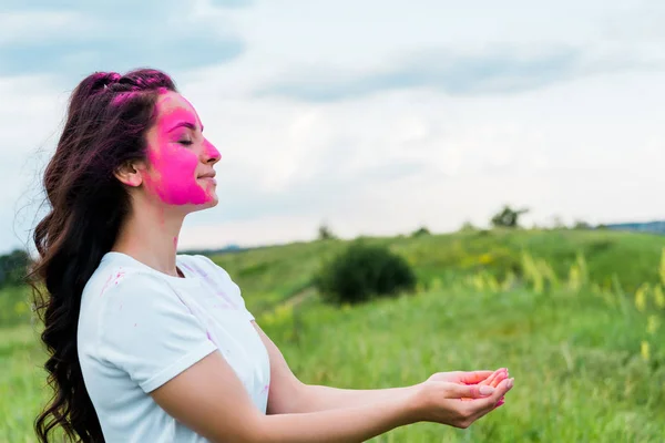 Mulher feliz com tinta holi rosa no rosto de pé com as mãos de chávena — Fotografia de Stock