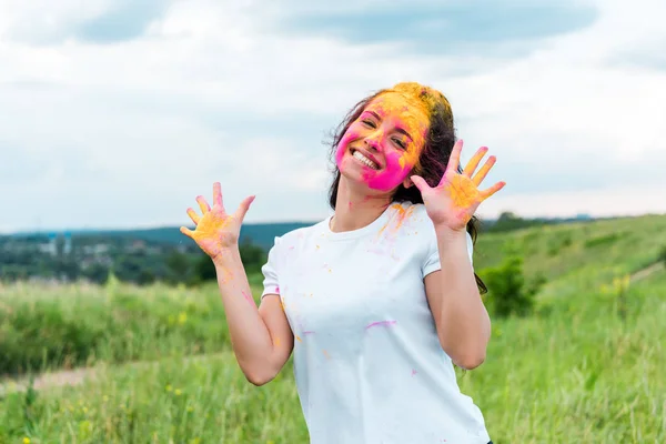 Happy woman with pink and yellow holi paint on face and hands — Stock Photo