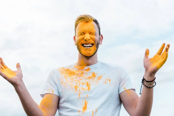 Homem feliz com olhos fechados e pintura holi amarelo no rosto — Fotografia de Stock