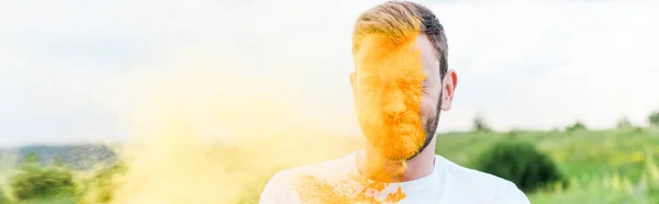 Панорамний знімок молодого чоловіка з закритими очима біля бризок жовтої фарби Холі — стокове фото