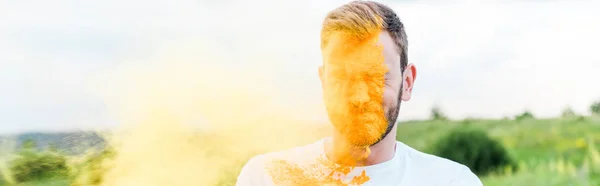 Panoramic shot of young man with closed eyes near splash of yellow holi paint — Stock Photo