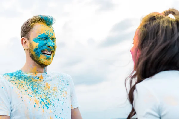 Selective focus of happy man with closed eyes and holi paint on face near woman — Stock Photo