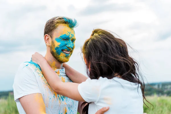 Selective focus of happy man with closed eyes and holi paint on face near young woman — Stock Photo