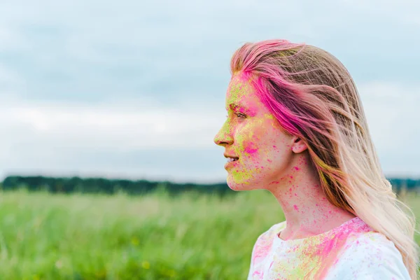 Seitenansicht einer glücklichen jungen Frau mit gelber und pinkfarbener Holi-Farbe im Gesicht — Stockfoto