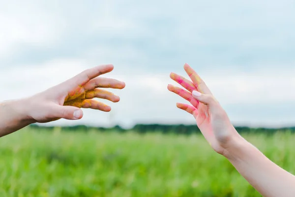 Cropped view of man and woman with holi paint on hands gesturing near blue sky — Stock Photo