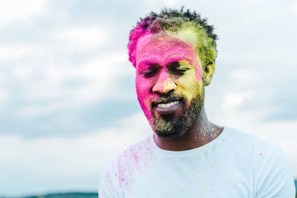 Homme afro-américain en t-shirt blanc et peintures holi colorées sur le visage — Photo de stock