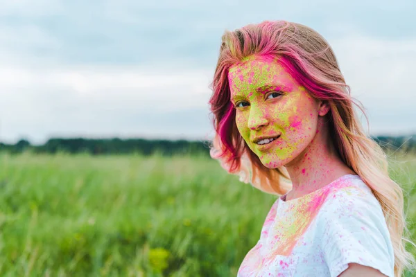 Happy young woman with green and pink holi paint on face — Stock Photo