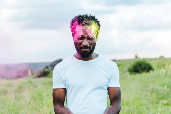 Afrikanisch-amerikanischer Mann mit geschlossenen Augen in weißem T-Shirt und bunten Holi-Farben im Gesicht — Stockfoto