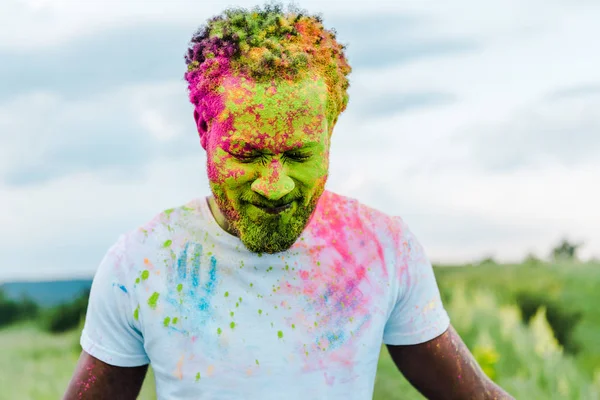 Happy african american man with colorful holi paints on face — Stock Photo