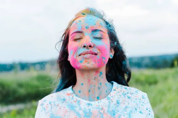 Positive woman with closed eyes and colorful holi paints on face — Stock Photo